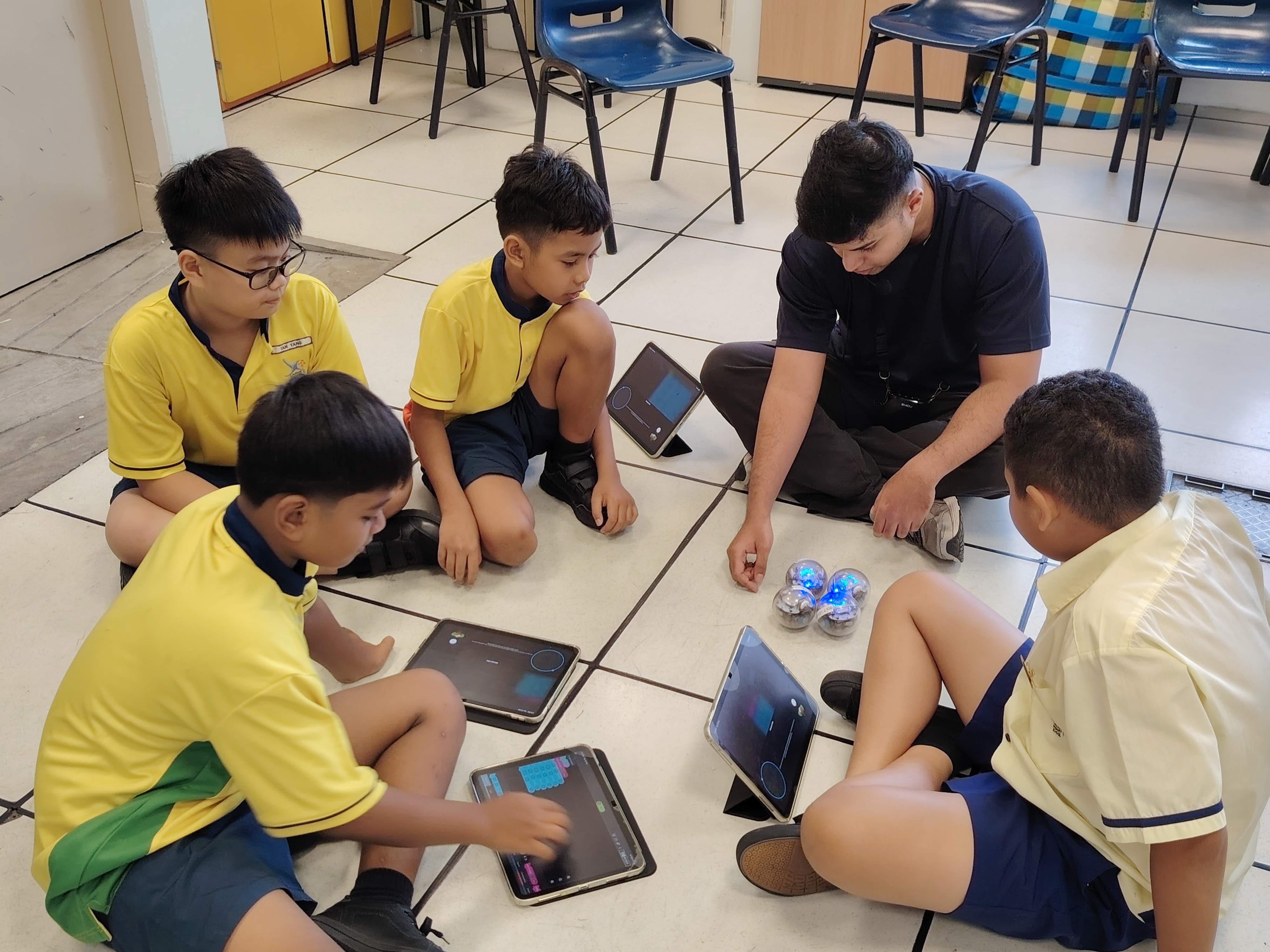 The CFF instructor, Mr Mikail sits with the students to teach them how to control the Spherobots